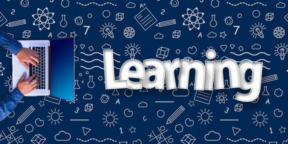 Hände schreiben auf einem Notebook neben einem Learning Schriftzug