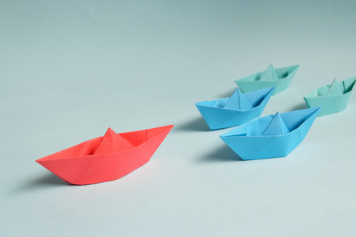 Kleine gefaltene Papierboote, die einem größeren Papierboot folgen