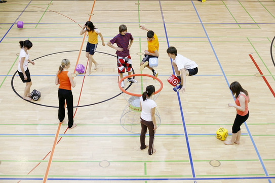 Kinder in einer Turnhalle, die mit übergroßen Schaumstoffwürfeln Übungen machen