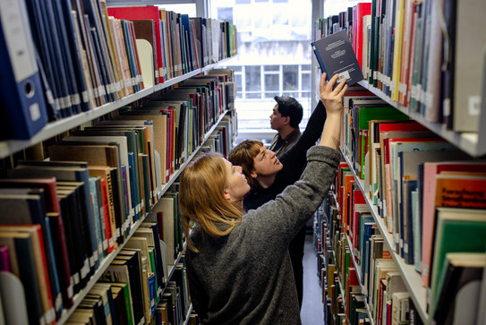 Studierende suchen nach Büchern in Bücherregalen in der Bibliothek.